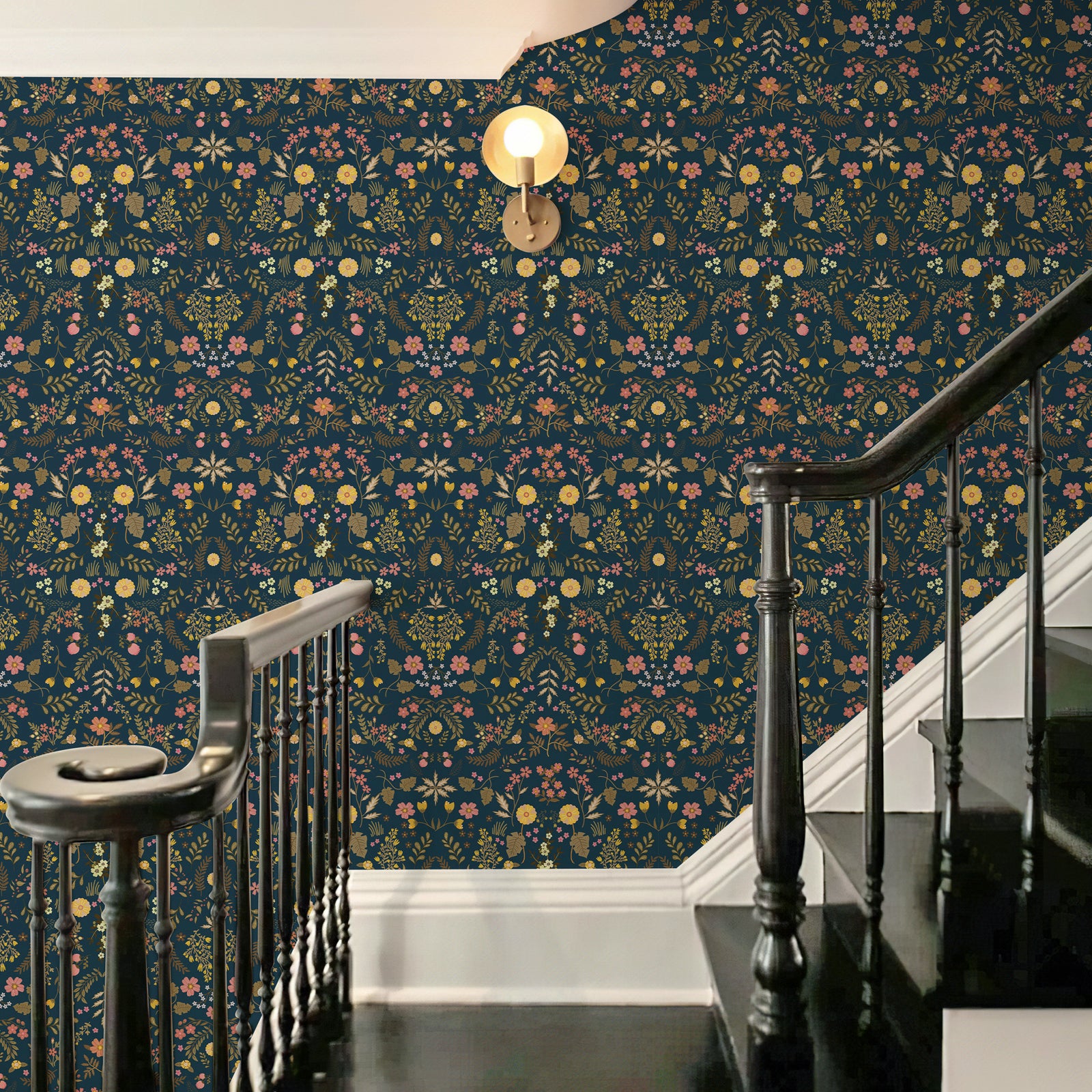 Vintage wildflower wallpaper decorates the stairwell wall. The rich floral pattern matches dark‑wood stair handrail, creating an elegant cottage‑style entryway atmosphere.