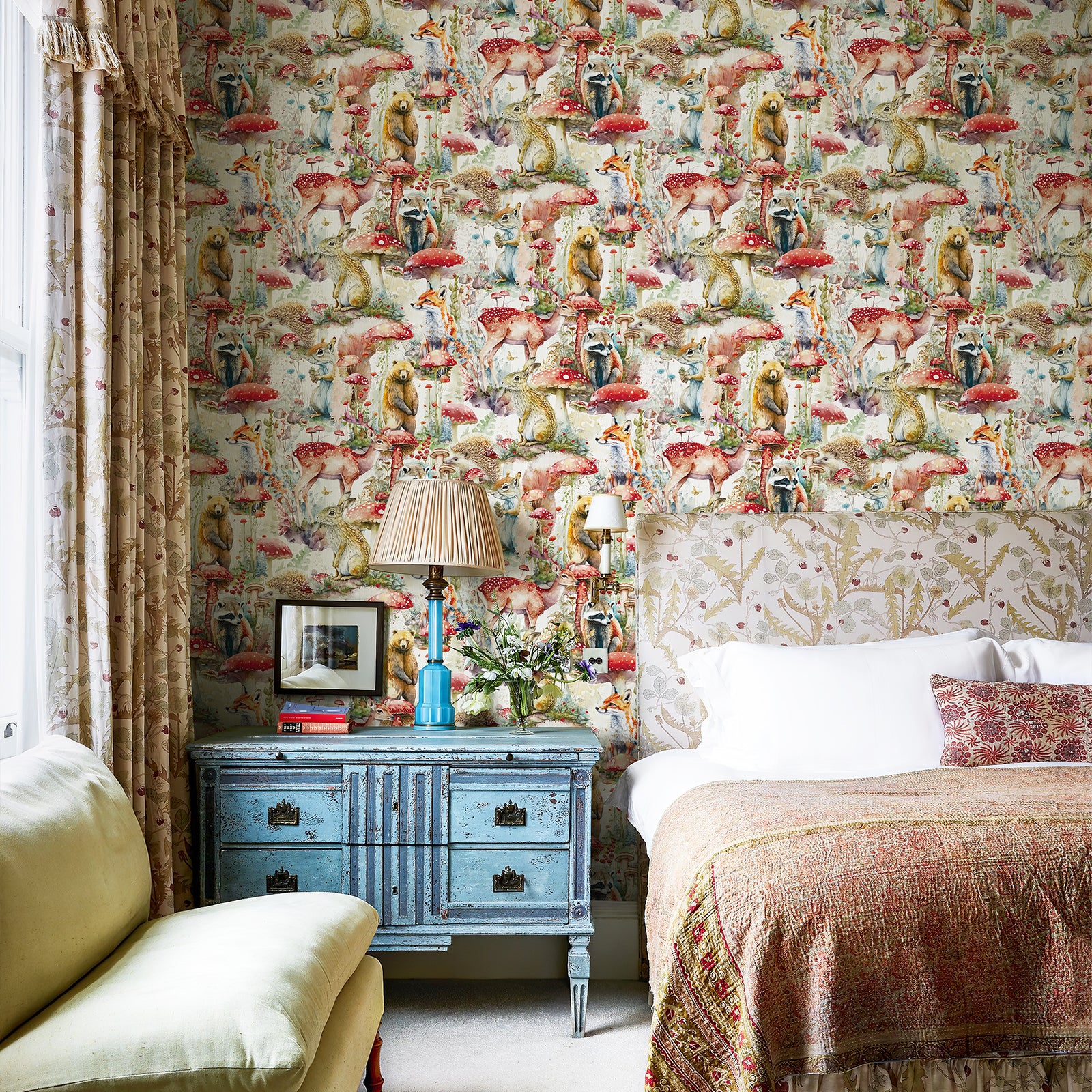 Storybook forest wallpaper applied as a full bedroom wall. It pairs with vintage nightstand, soft bedding and printed curtains for a cozy whimsical kids‑bedroom setting.